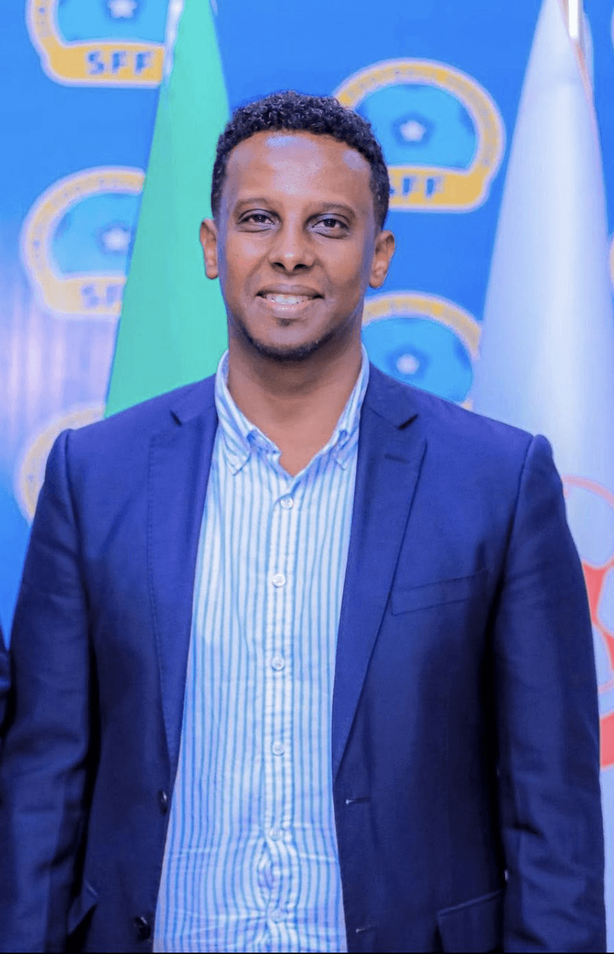 Deeq Afrika in a blue suit in front of the Somali Football Federation backdrop